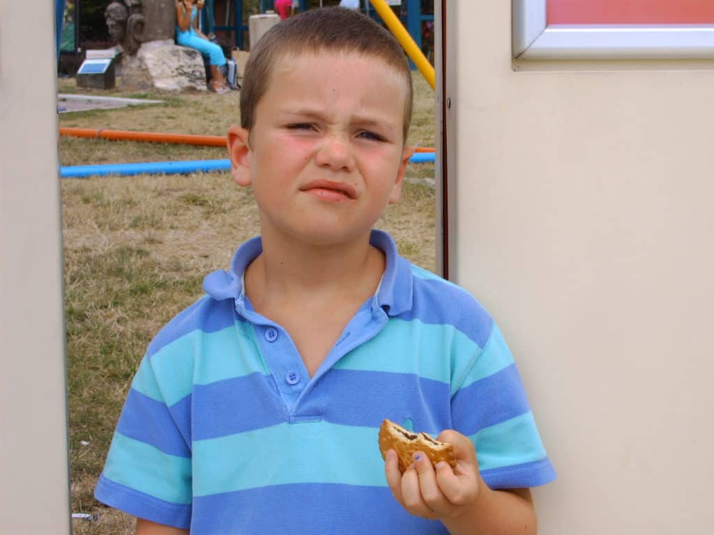 A 7-year-old kid holding some sort of cookie and looking weird