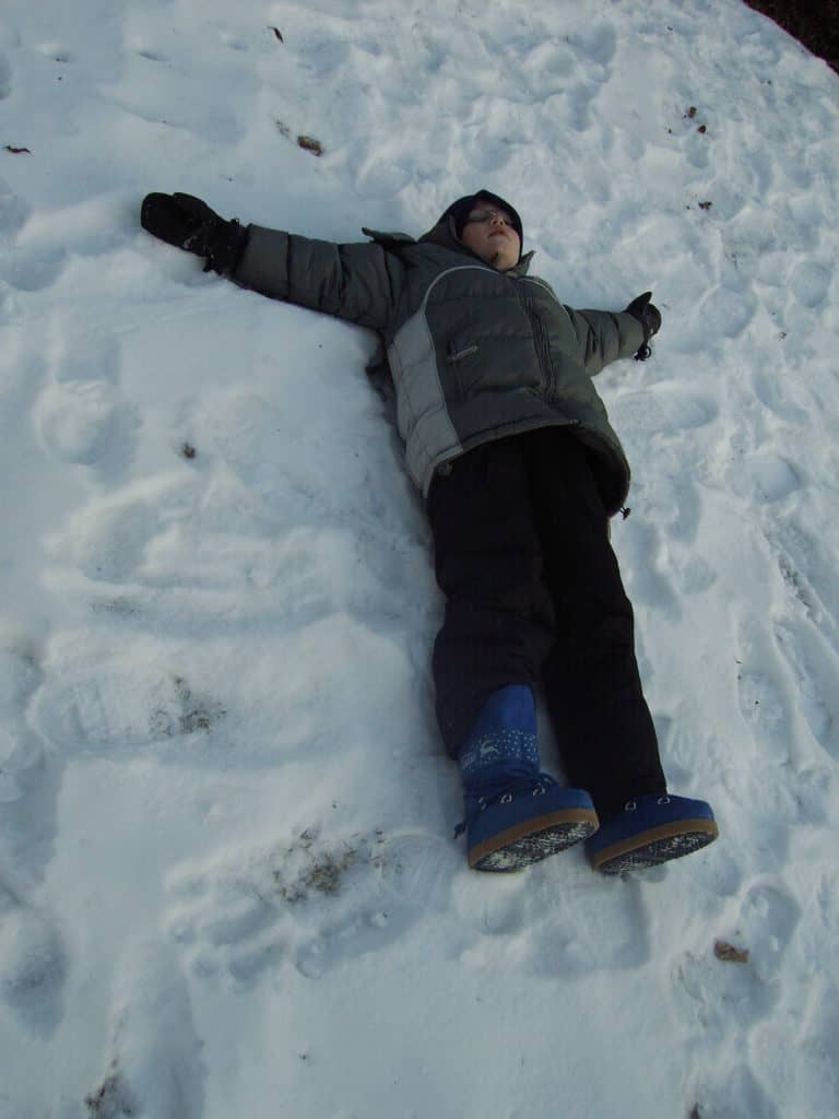 8-year-old laying in a bunch of snow making snow angels
