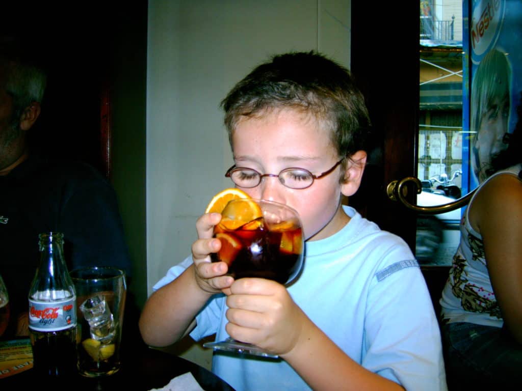 A dorky kid with glasses drinking his mom's sangria while his own cola light is literally right there