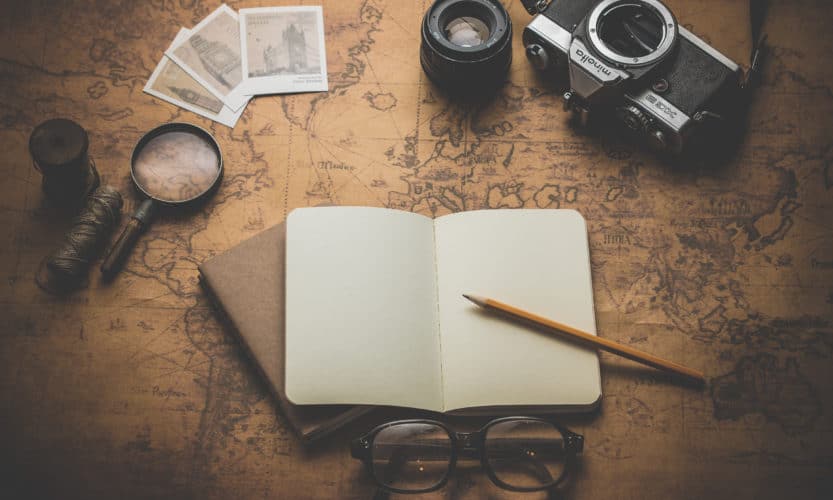 Notebook, camera, lens, magnifying glass and glasses on top of a world map