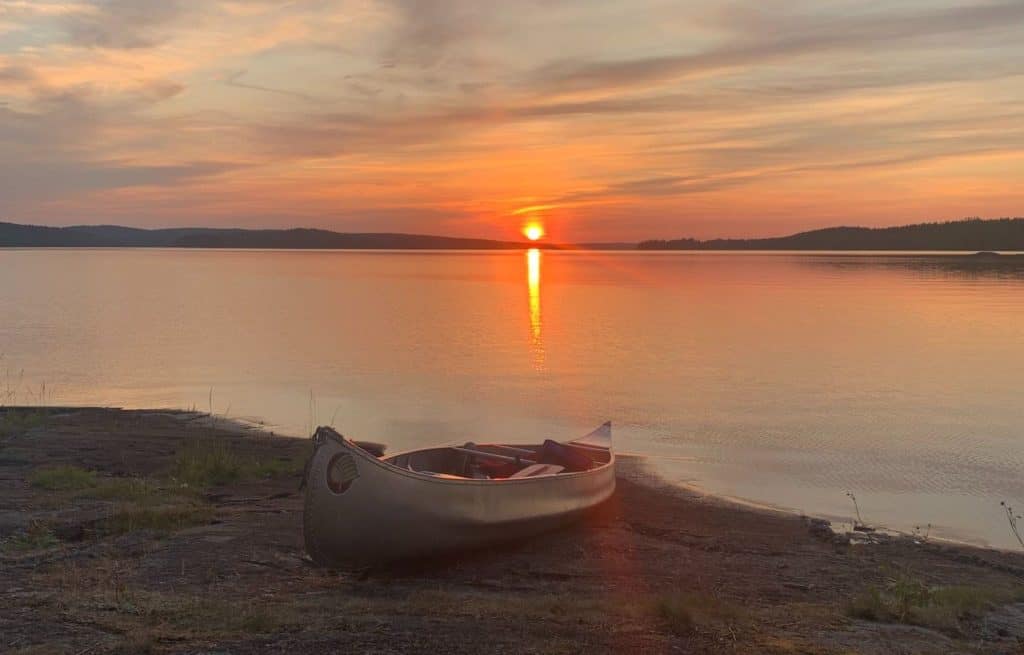 photo of an empty canoe on the shore, with the sun setting over the lake in the background